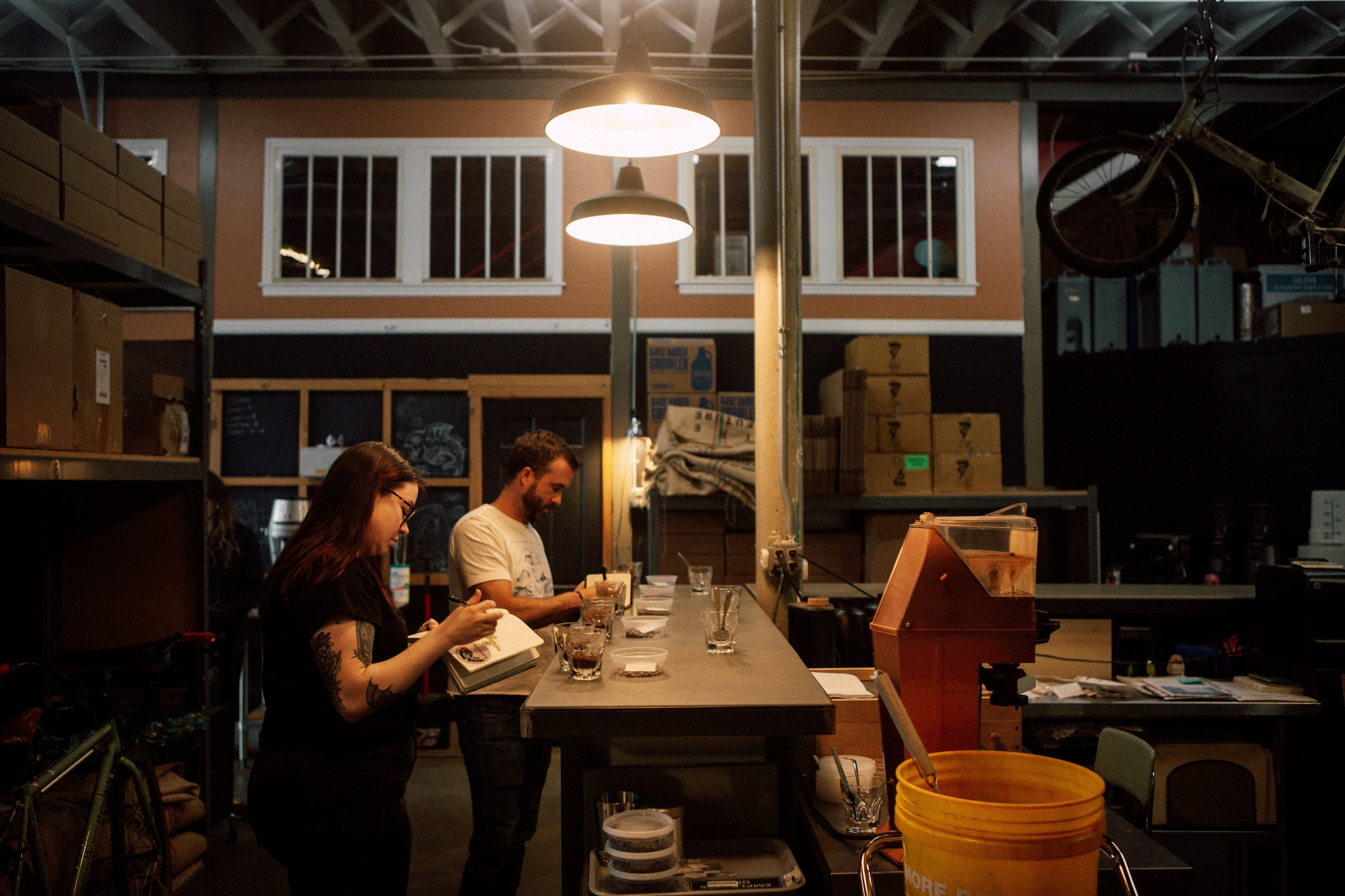Two people working at a table in a dimly lit room with various equipment and supplies.